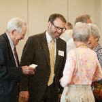 A man chuckles, while a smiling man is inclining towards a smiling woman and a second woman whose face cannot be seen